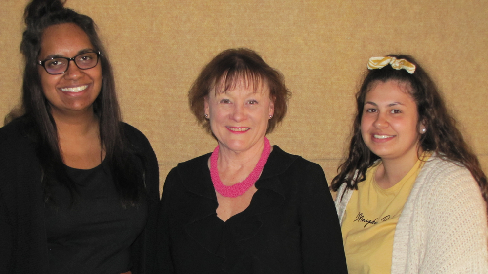 Three women standing in a line in front of a yellow wall